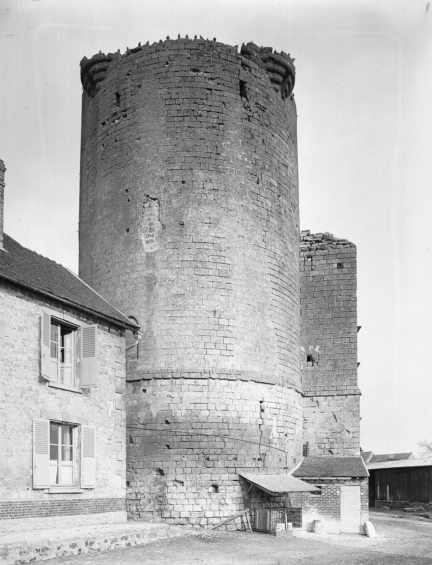Photographie en noir et blanc. Tour ronde accolée à une maison.
