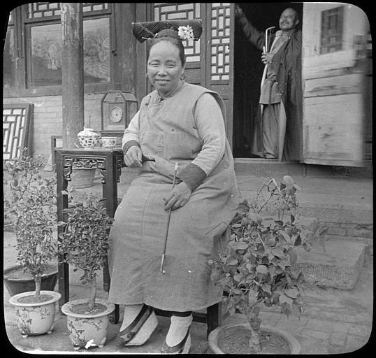 Témoignage de la présence européenne en Chine, vers 1905,  Couple de chinois devant leur maison : femme posant avec une pipe à opium