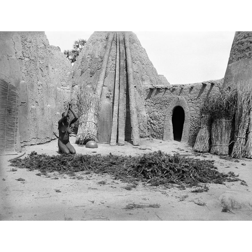 Marc Allégret, Jeune femme agenouillée devant des racines, entourée de cases en pisé, appelées tolek, 1925-1926