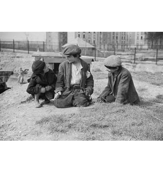 3 jeunes garçons assis par terre. En contre-bas, en arrière plan, des roulottes.