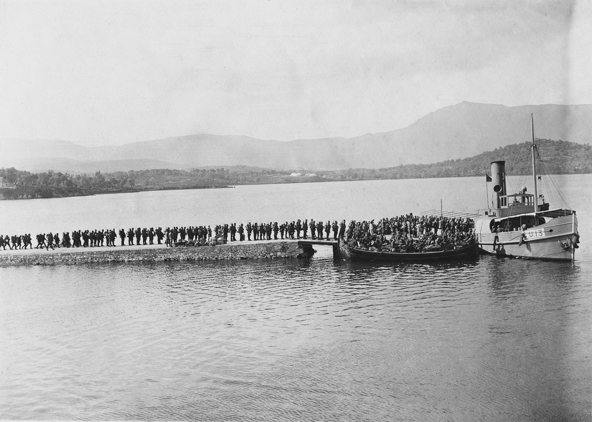 Une longue file de soldats sur une jetée attendent pour embarquer sur des chaloupes. 